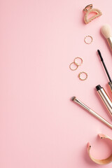 Make up beauty concept. Top view vertical photo of gold rings bracelet makeup brushes mascara and barrette on pastel pink background with copyspace