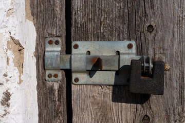 Old padlock, latch on wooden door with cracked texture. Close-up