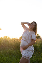 Naklejka na ściany i meble tender pregnancy portrait on sunset. expecting mother to be outside in pink dress. Beautiful tender mood photo of pregnancy.