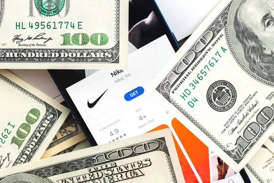Nike shopping app logo on mobile phone screen. Business background with laptop and money photo