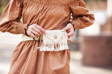 Young lady wearing brown dress with macrame belt bag, posing in street of european city. Outdoor. Copy, empty space for text - obrazy, fototapety, plakaty