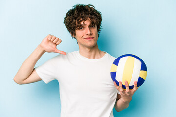 Young caucasian man playing volleyball isolated on blue background feels proud and self confident,...