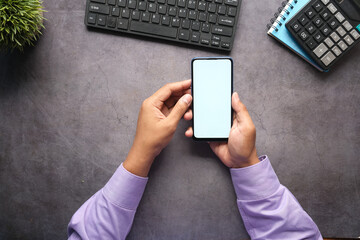 Top view of man hand holding smart phone with empty screen on office desk 