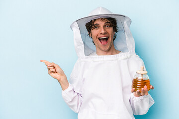 Young caucasian beekeeper man isolated on blue background smiling and pointing aside, showing...