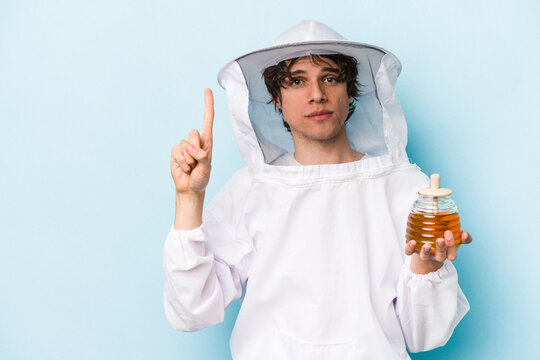 Young caucasian beekeeper man isolated on blue background showing number one with finger.