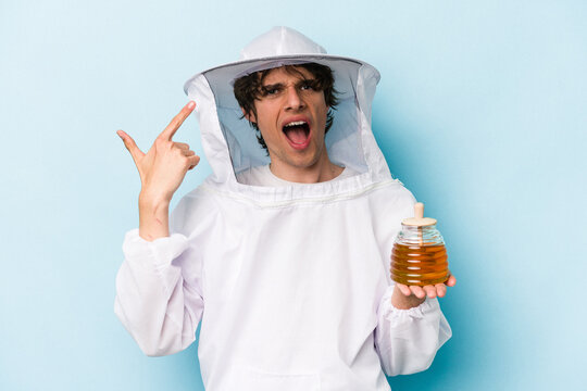 Young caucasian beekeeper man isolated on blue background showing a disappointment gesture with forefinger.