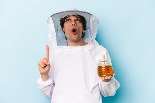 Young caucasian beekeeper man isolated on blue background pointing upside with opened mouth.