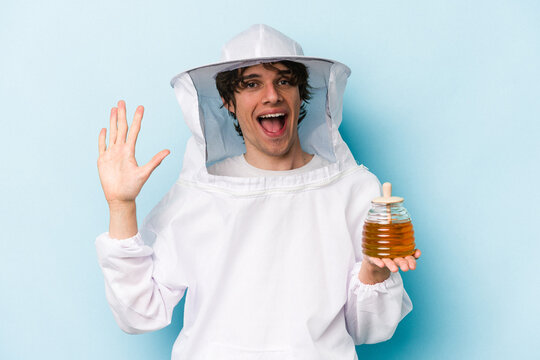Young caucasian beekeeper man isolated on blue background smiling cheerful showing number five with fingers.