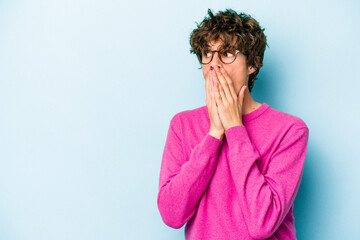 Young caucasian man isolated on blue background thoughtful looking to a copy space covering mouth with hand.