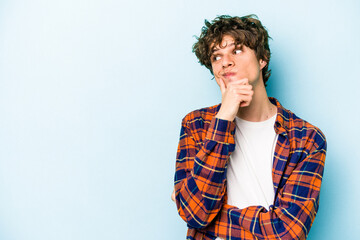 Young caucasian man isolated on blue background looking sideways with doubtful and skeptical...