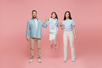 Fototapeta premium Full body young smiling cool happy parents mom dad with child kid daughter teen girl in blue clothes hold hands jump high have fun isolated on plain pastel light pink background. Family day concept.