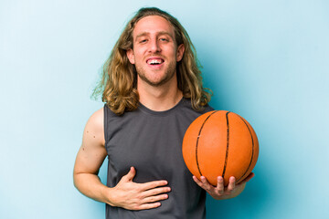 Young caucasian man playing basketball isolated on blue background laughing and having fun.