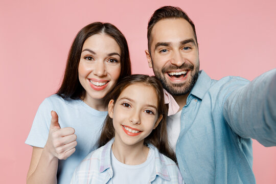 Close up young happy smiling parents mom dad with child kid daughter teen girl in blue clothes doing selfie shot pov on mobile cell phone show thumb up isolated on plain pastel light pink background