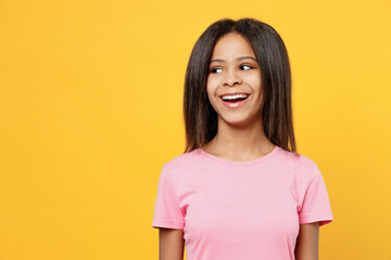 Little fun kid girl of African American ethnicity 12-13 years old in pink t-shirt look aside on workspace area mock up isolated on plain yellow background studio portrait. Childhood lifestyle concept.