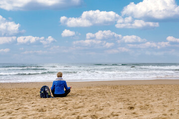 Meditation by the sea. Woman sitting on the beach practicing meditation observing the horizon of...