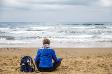Meditation by the sea. Woman sitting on the beach practicing meditation observing the horizon of...