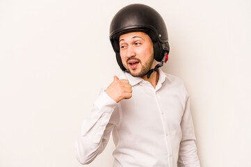 Hispanic business man going to work with motorcycle isolated on white background points with thumb finger away, laughing and carefree.