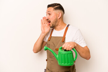 Gardener hispanic man holding a watering can isolated on white background shouting and holding palm near opened mouth.