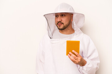 Hispanic beekeeper man holding honey isolated on white background relaxed thinking about something looking at a copy space.