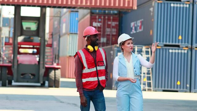 Caucasian business female and black male dock worker working control loading Containers box from Cargo at warehouse container yard.
