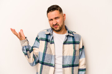 Young hispanic man isolated on white background doubting and shrugging shoulders in questioning gesture.