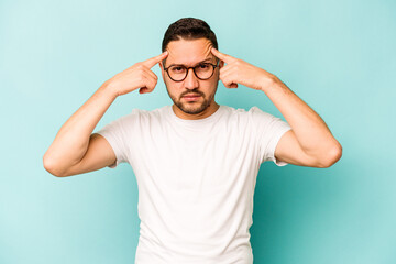 Young hispanic man isolated on blue background focused on a task, keeping forefingers pointing head.