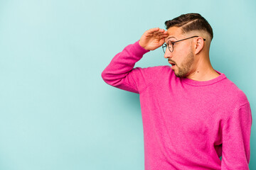 Young hispanic man isolated on blue background looking far away keeping hand on forehead.