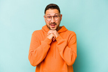 Fototapeta premium Young hispanic man isolated on blue background praying for luck, amazed and opening mouth looking to front.