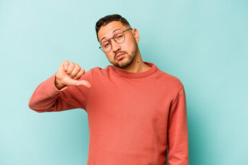 Young hispanic man isolated on blue background showing a dislike gesture, thumbs down. Disagreement...