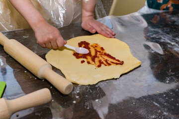 child cook prepares pizza, the dough is smeared with tomato sauce