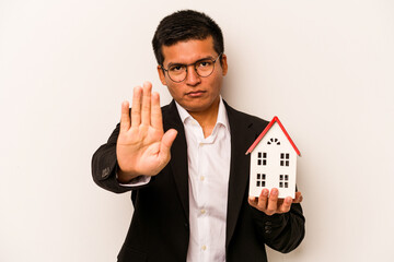 Young business hispanic man holding a little house isolated on white background standing with...