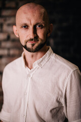 Portrait of a bald man with a beautiful beard in a white shirt on a brick background