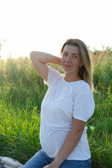 cute pregnancy portrait. happy mother to be with a big belly in white t-shirt and jeans outside on the meadow at sunset