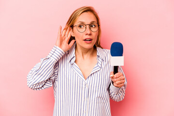 Young caucasian TV presenter woman isolated on pink background trying to listening a gossip. - obrazy, fototapety, plakaty