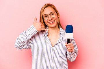 Young caucasian TV presenter woman isolated on pink background showing a mobile phone call gesture with fingers.