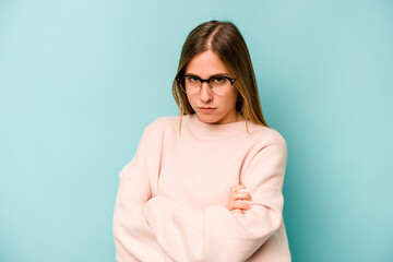 Young caucasian woman isolated on blue background frowning face in displeasure, keeps arms folded.