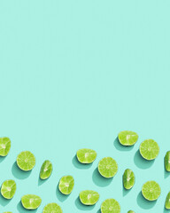 Citrus lime fruit as creative background, slices of green lime with hard shadows at sunlight on pastel mint background with copy space. Fruits food concept. Top view, monochrome colored