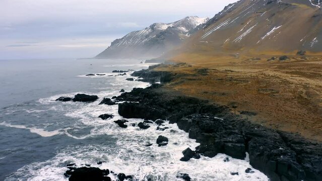 Rocky Coast washed by ocean waves. Aerial view of a black beach mossy Mountains in Iceland. Untouched Arctic Nature.