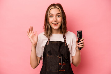 Young hairdresser woman holding scissors isolated on pink background receiving a pleasant surprise,...