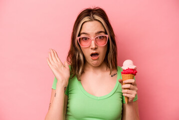 Young caucasian woman holding an ice cream isolated on pink background surprised and shocked.