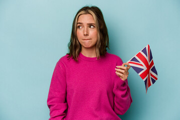 Young caucasian woman holding a English flag isolated on blue background confused, feels doubtful...