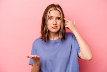 Young caucasian woman isolated on pink background holding and showing a product on hand.