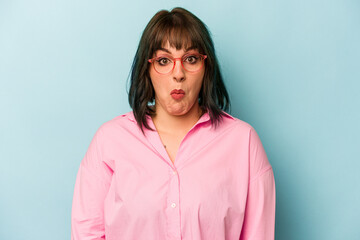 Young caucasian woman isolated on blue background shrugs shoulders and open eyes confused.