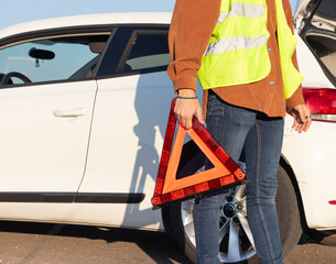 unrecognizable man holding a red triangle on the road with broken car and breakdown concept