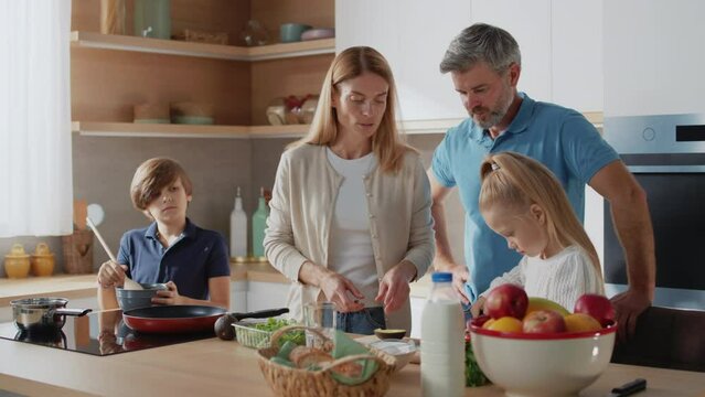 Caucasian family with little kids prepare together healthy vegetable salad in the kitchen at home. Parents teach little daughter healthy habits and how to cut avocado.