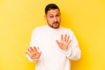 Young hispanic man isolated on yellow background rejecting someone showing a gesture of disgust.