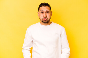 Young hispanic man isolated on yellow background blows cheeks, has tired expression. Facial expression concept.