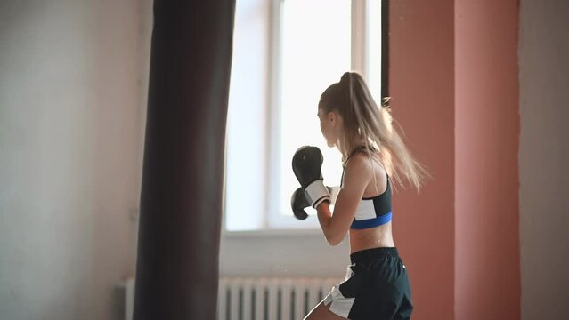 Beautiful kickboxing woman training punching bag in fitness studio.