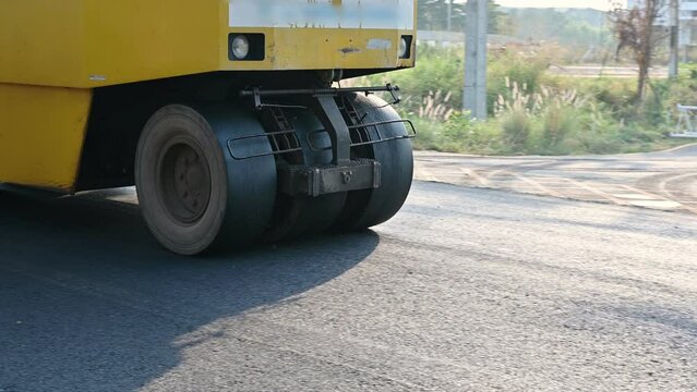 Yellow steamroller or soil compactor working on asphalt road at construction site