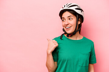 Young caucasian woman wearing helmet isolated on pink background points with thumb finger away, laughing and carefree.